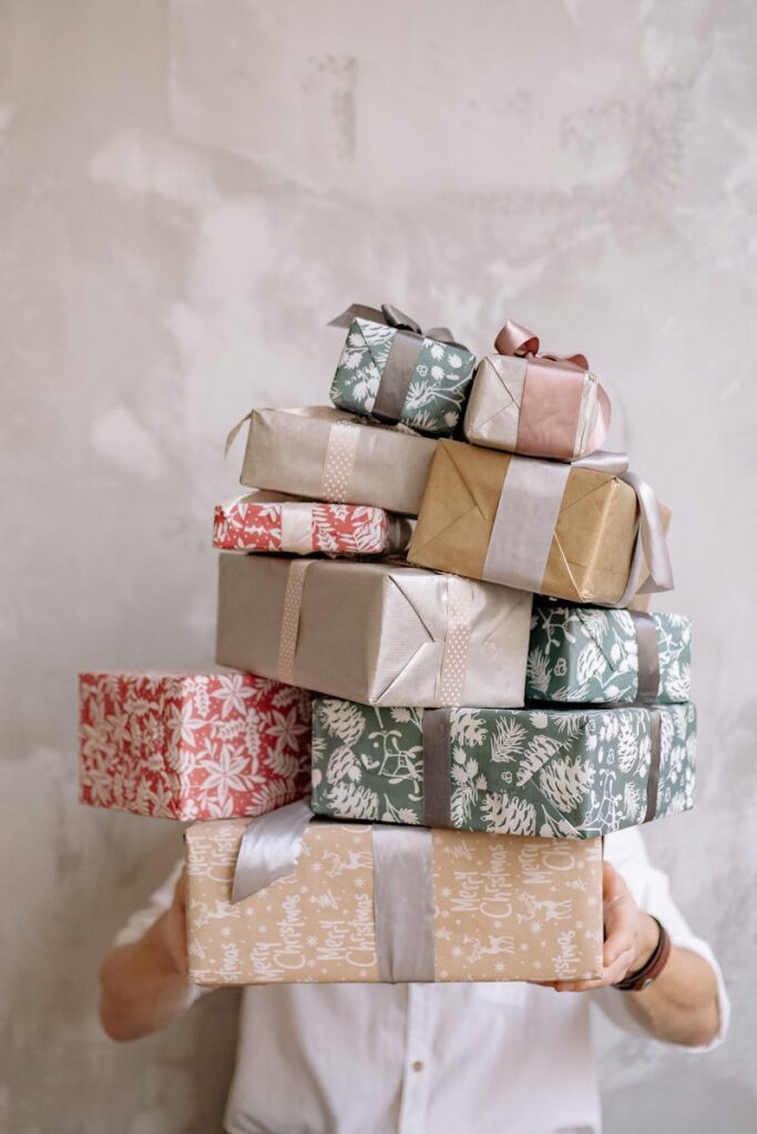 pexels-photo-6209315-6209315 Person hiding behind a tall stack of gift-wrapped boxes against a gray wall, indoors.